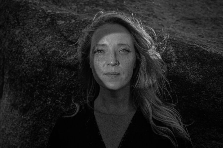 Black and white image of Ceara Conway. Long blonde hair, blowing in the wind with landscape back drop.